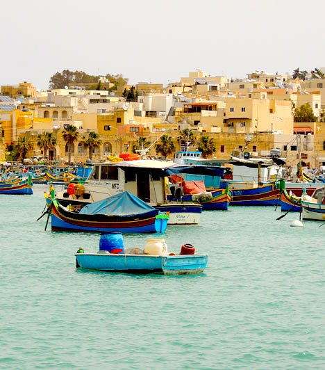  	Dél-máltai városka kikötője  	Városi kikötő Málta déli részén, Marsaxlokkban, tipikus színes halászcsónakokkal. A helyiek gazdálkodnak, halásznak vagy éppen a turisták által igen kedvelt kávézókban és trafikokban dolgoznak. Minden kissé lelassult, senki sem siet, hosszas párbeszédek és vidám hangzavar keveredik a mindig susogó szél hangjával. Málta vidéki részén jócskán kevesebb a turista, mint a fővárosban, Vallettában, így valódi kikapcsolódás belesni a sziget bármelyik kisvárosának átlagos hétköznapjaiba.