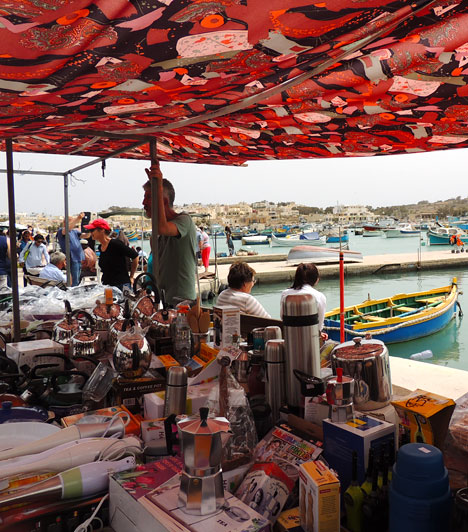  	Piac, kikötő, pihenőhely egyben  	Marsaxlokkon a kikötő melletti partrész nem csak a halászcsónakok tároló helyeként és pálmafákkal szegélyezett sétányként szolgál, hanem kávézók tucatjai fogják körbe, de itt árulják portékáikat a helyi kiskereskedők és gazdák is, akik jól megférnek a szuveníreket kínáló árusokkal.